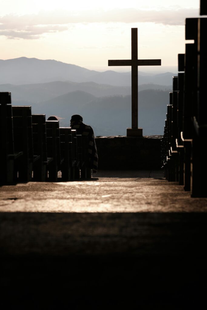 A serene mountain setting with a prominent cross and benches at sunset, evoking peace and reflection.